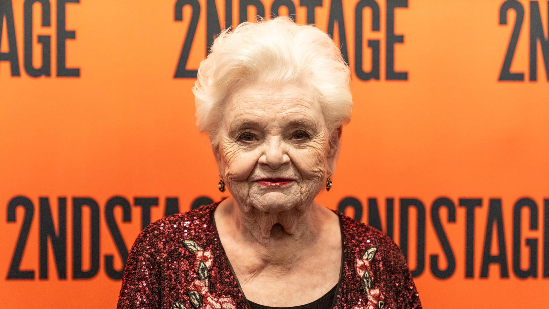 Schasuspielerin June Squibb steht vor einer orangen Wand. 