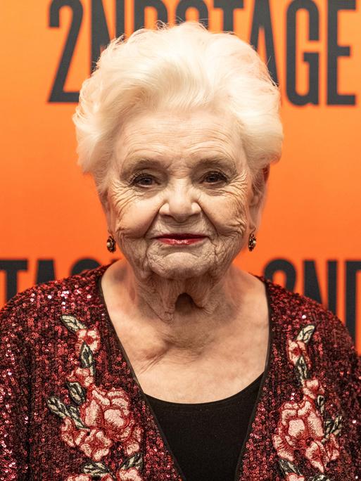 Schasuspielerin June Squibb steht vor einer orangen Wand. 