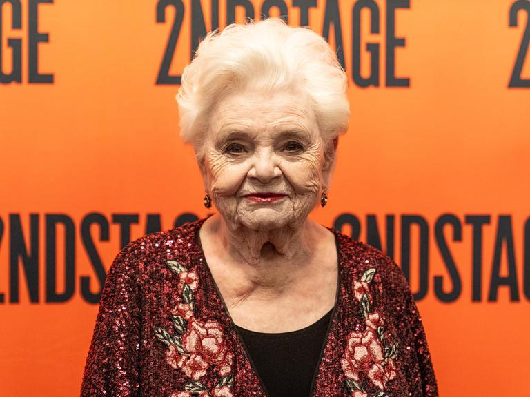 Schasuspielerin June Squibb steht vor einer orangen Wand. 