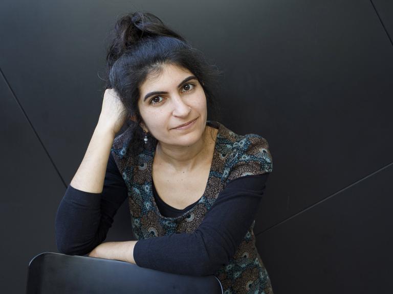 Shida Bazyar sitzt vor einem schwarzen Hintergrund und blickt in die Kamera. Sie hat ihren Kopf auf ihrer rechten Hand aufgestützt Shida Bazyar sitzt vor einem schwarzen Hintergrund und blickt in die Kamera. Sie hat ihren Kopf auf ihrer rechten Hand aufgestützt