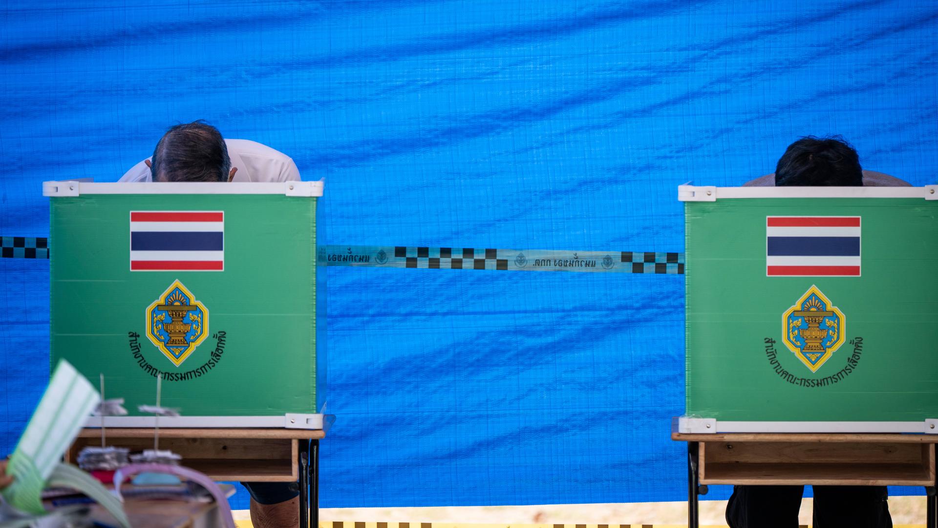 In einem Wahllokal in Bangkok sieht man zwei Kabinen, in denen Bürger, abgeschottet und mit gesenktem Kopf, ihre Wahl treffen. In einem Wahllokal in Bangkok sieht man zwei Kabinen, in denen Bürger, abgeschottet und mit gesenktem Kopf, ihre Wahl treffen.