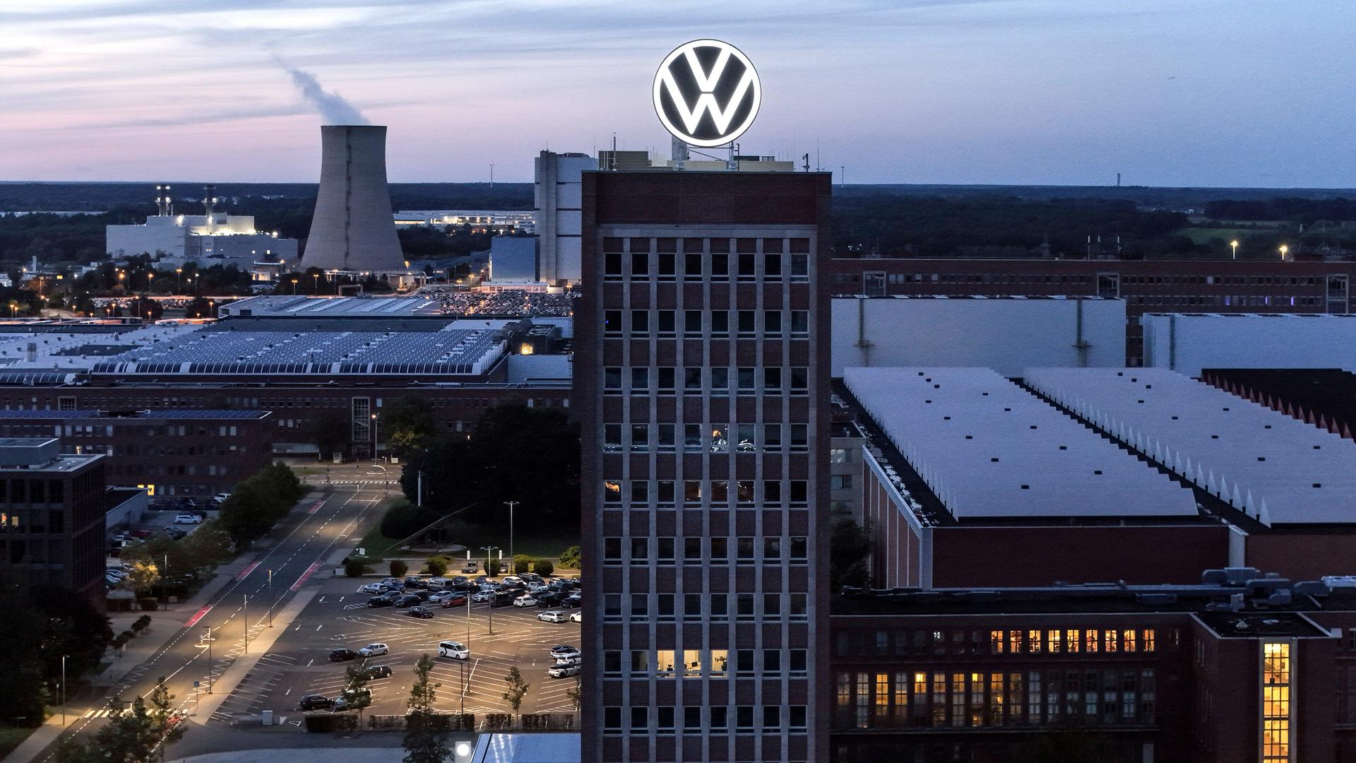 Eine Industrieanlage liegt in der Dunkelheit. Im Hintergrund dampf es aus einem Kühlturm, auf einem Hochhaus im Vordergrund prankgt ein Firmenlogo.