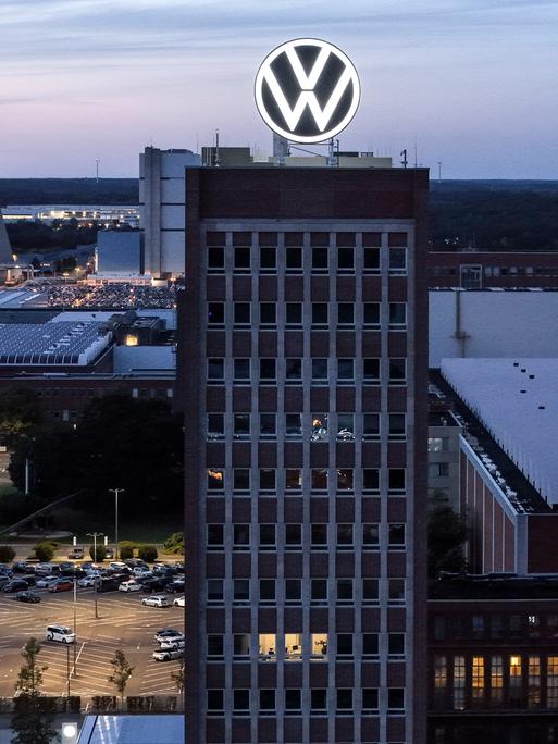 Eine Industrieanlage liegt in der Dunkelheit. Im Hintergrund dampf es aus einem Kühlturm, auf einem Hochhaus im Vordergrund prankgt ein Firmenlogo.