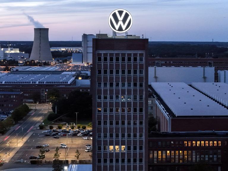 Eine Industrieanlage liegt in der Dunkelheit. Im Hintergrund dampf es aus einem Kühlturm, auf einem Hochhaus im Vordergrund prankgt ein Firmenlogo.