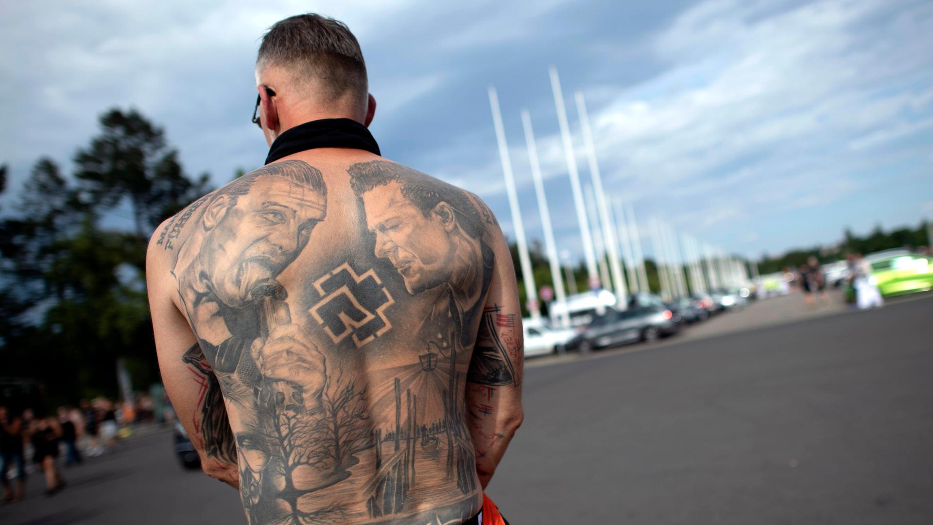 Rückenansicht eines männlichen Fan mit freiem Oberkörper, trägt als Tattoo das Konterfei von Till Lindemann auf seinem nackten Rücken, beim Besuch des Rammstein-Konzerts vor dem Berliner Olympiastadion im Juli 2023. 