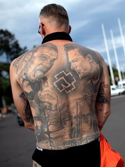Rückenansicht eines männlichen Fan mit freiem Oberkörper, trägt als Tattoo das Konterfei von Till Lindemann auf seinem nackten Rücken, beim Besuch des Rammstein-Konzerts vor dem Berliner Olympiastadion im Juli 2023. 
