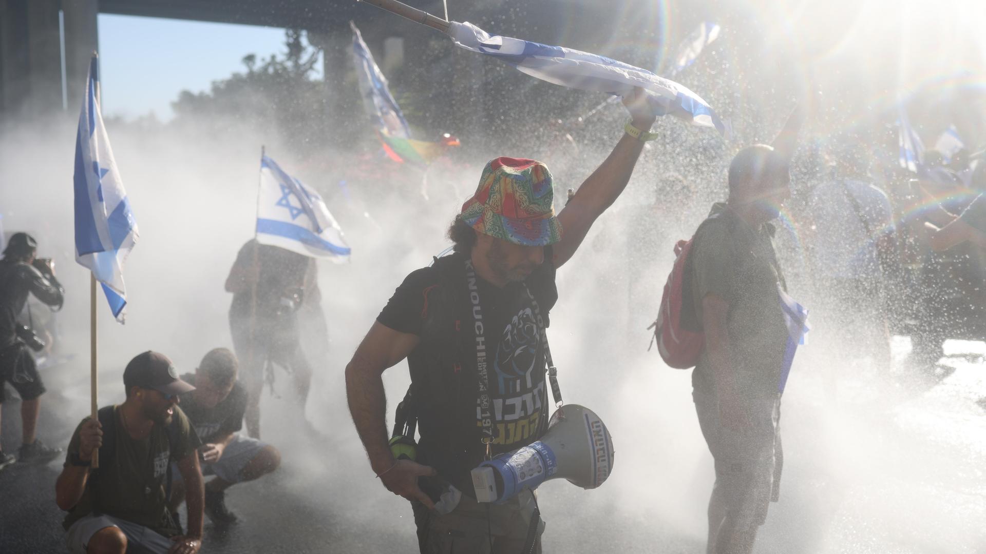 Israelische Demonstranten vor der Knesset im Regen von Wasserwerfern der Polizei. 