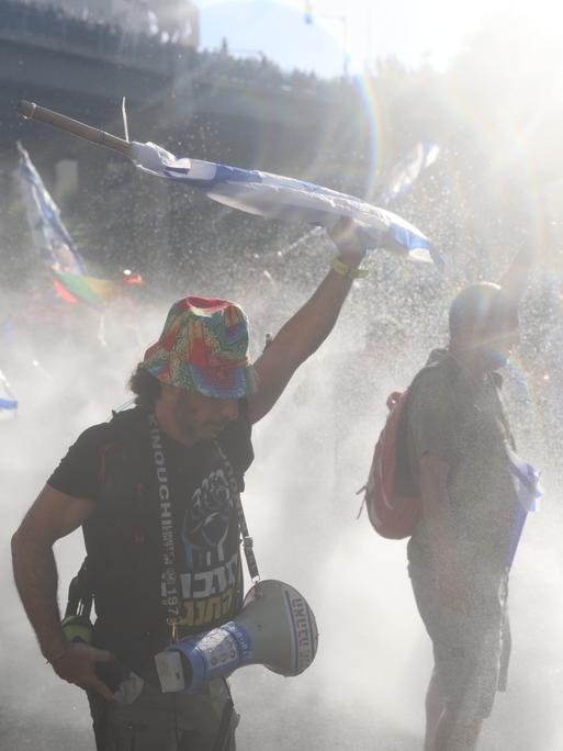 Israelische Demonstranten vor der Knesset im Regen von Wasserwerfern der Polizei. 