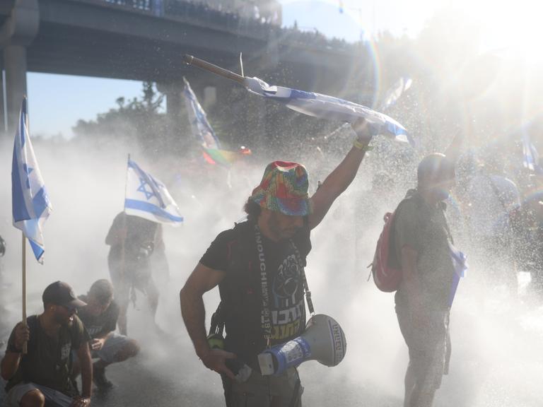 Israelische Demonstranten vor der Knesset im Regen von Wasserwerfern der Polizei. 