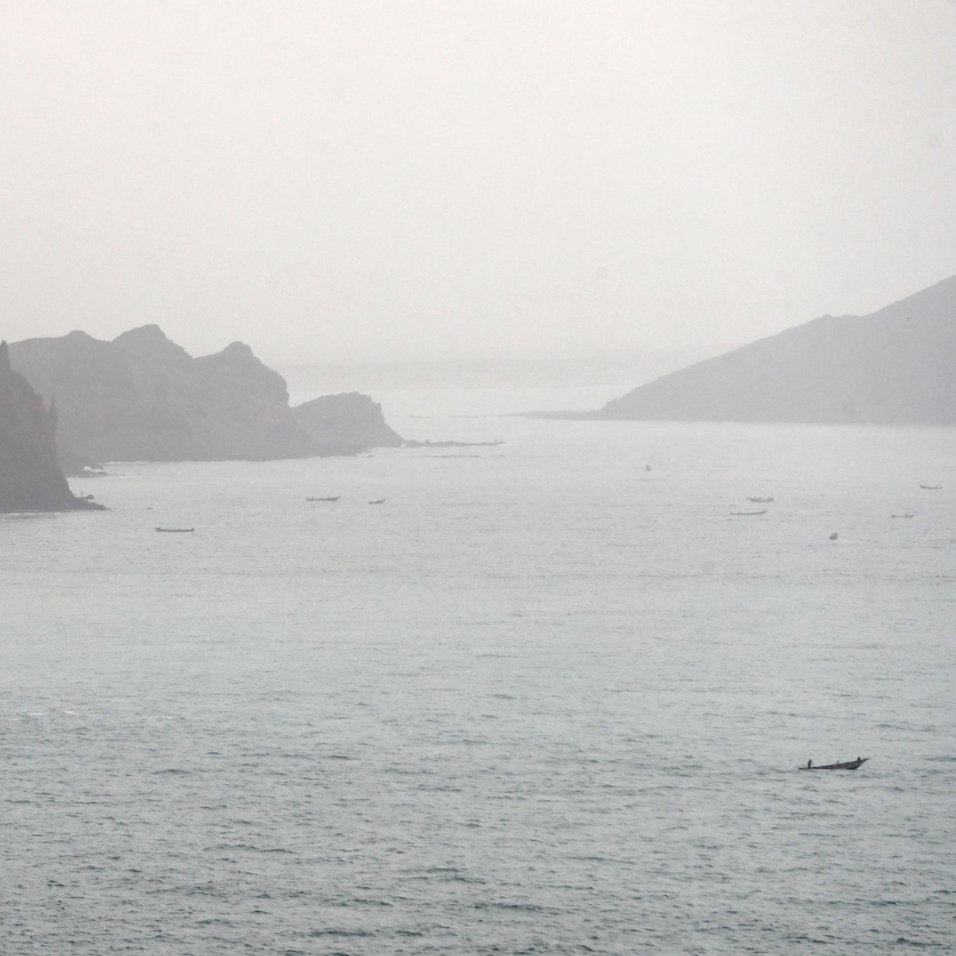 Links und rechts hohe Felsen, auf dem Wasser einige Fischerboote.
