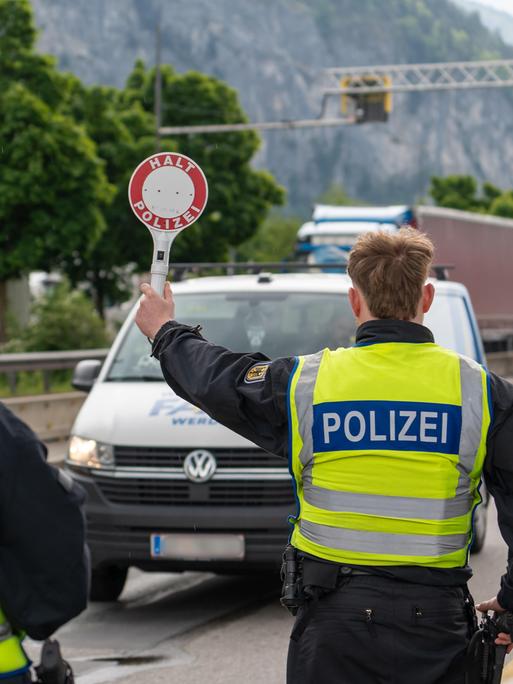 Ein Polizist stoppt ein Fahrzeug auf der Autobahn mit einer Polizeikelle mit der Aufschrift: "Halt Polizei". Neben ihm steht ein anderer Polizist.
