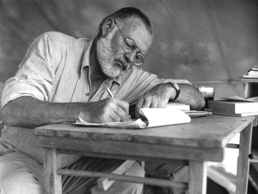 Der amerikanische Schriftsteller Ernest Hemingway (1899–1961) bei der Schreibarbeit an einem Klapptisch während einer Großwildjagd in Kenia, September 1952.