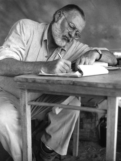 Der amerikanische Schriftsteller Ernest Hemingway (1899–1961) bei der Schreibarbeit an einem Klapptisch während einer Großwildjagd in Kenia, September 1952.