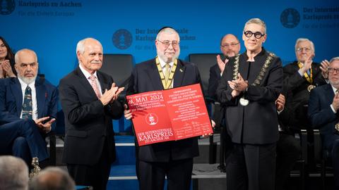 Jürgen Linden, Vorsitzender Karlspreis Direktorium (li.) und Sibylle Keupen Oberbürgermeisterin der Stadt Aachen (r.) überreichen den Karlspreises an Oberrabbiner Pinchas Goldschmidt. Er hält die Urkunde in seinen Händen.