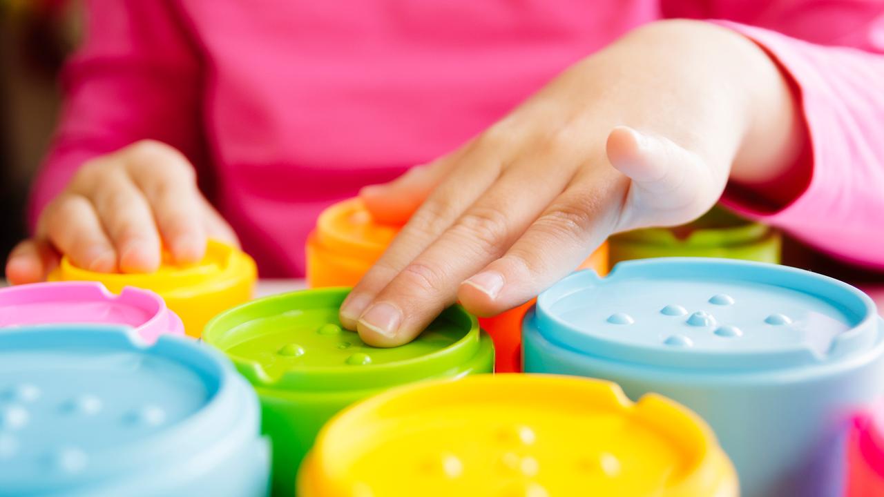 Ein Kind streicht mit den Händen über bunte Spielzeug-Becher. 