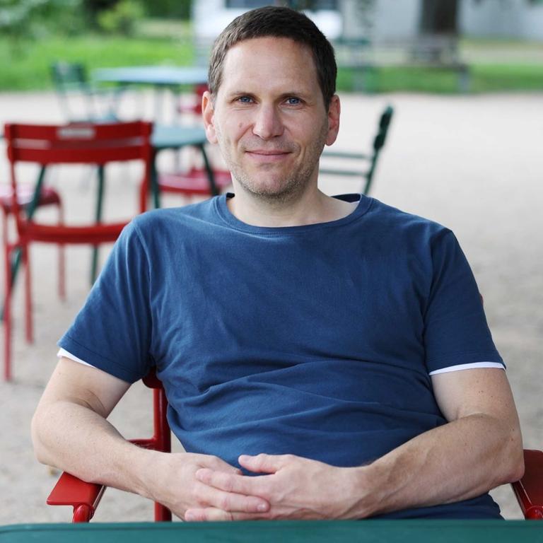 Peter Hofmann. Ein Mann mit kurzen dunklen Haaren sitzt auf einem Gartenstuhl.