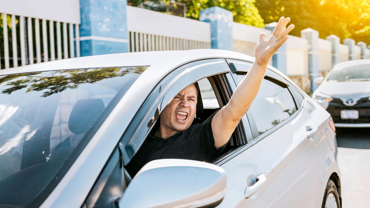 Ein wütender Fahrer schreit einen anderen Verkehrsteilnehmer aus dem Auto heraus an und gestikuliert durch das Fenster heraus.