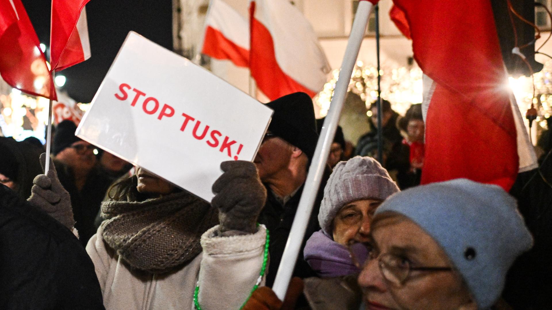 Menschen halten polnische Fahnen und Protestschilder in die Höhe, auf einem steht "Stop Tusk"