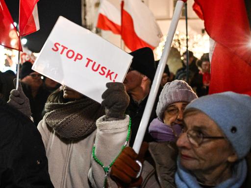 Menschen halten polnische Fahnen und Protestschilder in die Höhe, auf einem steht "Stop Tusk"
