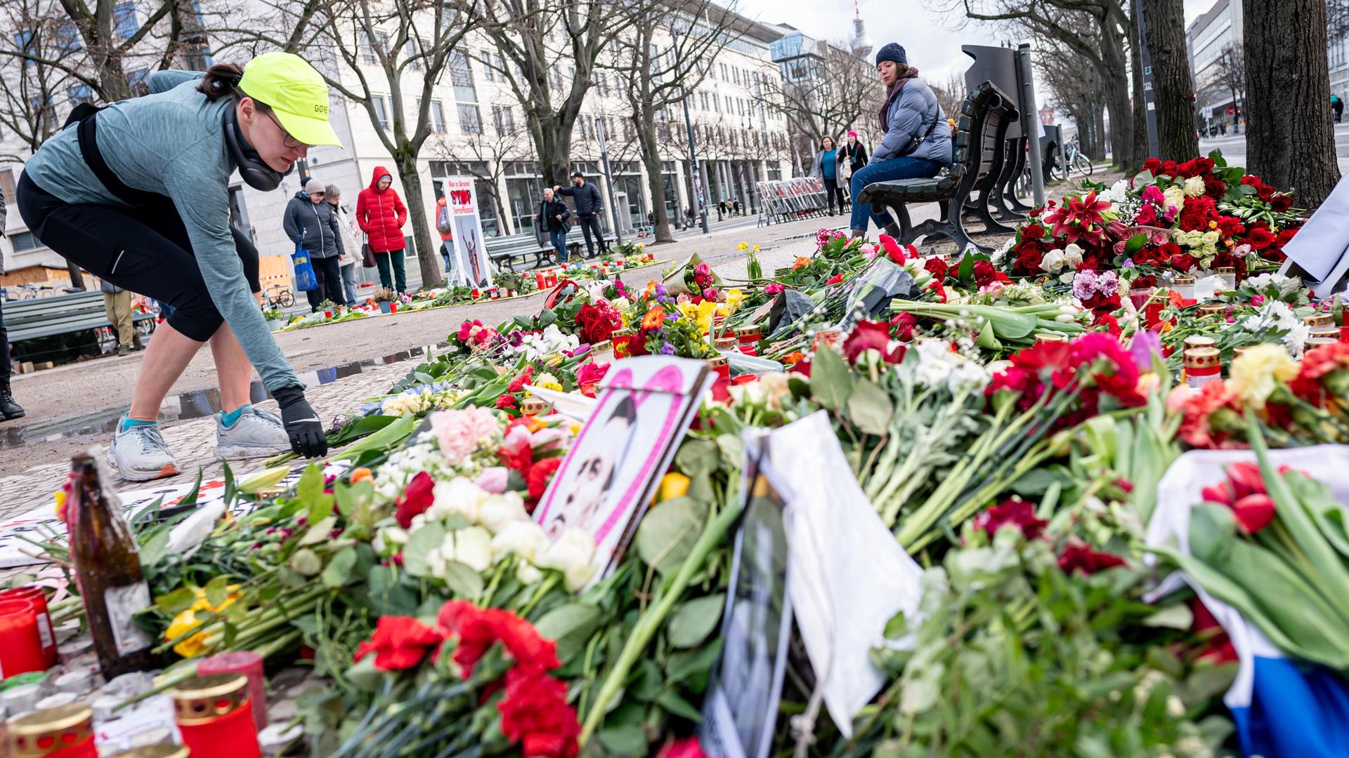 Eine Frau legt nach dem Tod Nawalnys vor der russischen Botschaft in Berlin Blumen nieder. Zahlreiche Blumensträuße liegen bereits dort, ebenso Bilder, die den Oppositionspolitiker zeigen, und Kerzen.