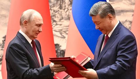Der russische Präsident Wladimir Putin (links) und der chinesische Präsident Xi Jinping stehen sich gegenüber, sie halten beide Dokumente in der Hand.  