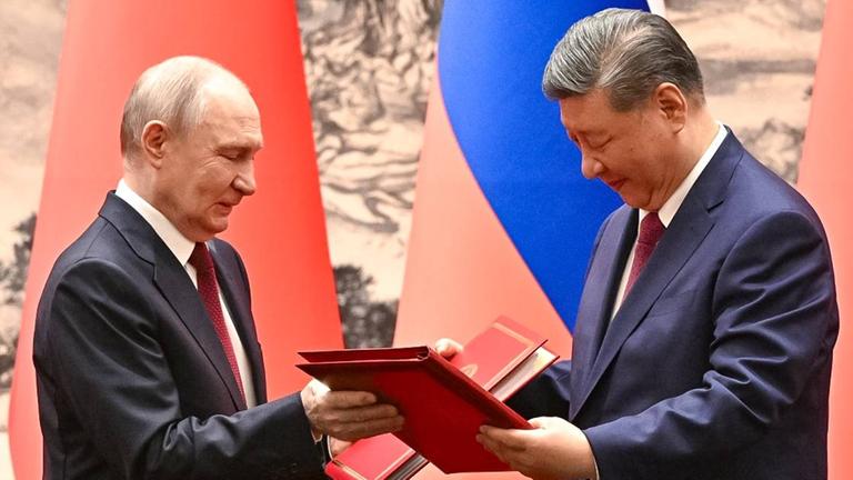 Der russische Präsident Wladimir Putin (links) und der chinesische Präsident Xi Jinping stehen sich gegenüber, sie halten beide Dokumente in der Hand.  