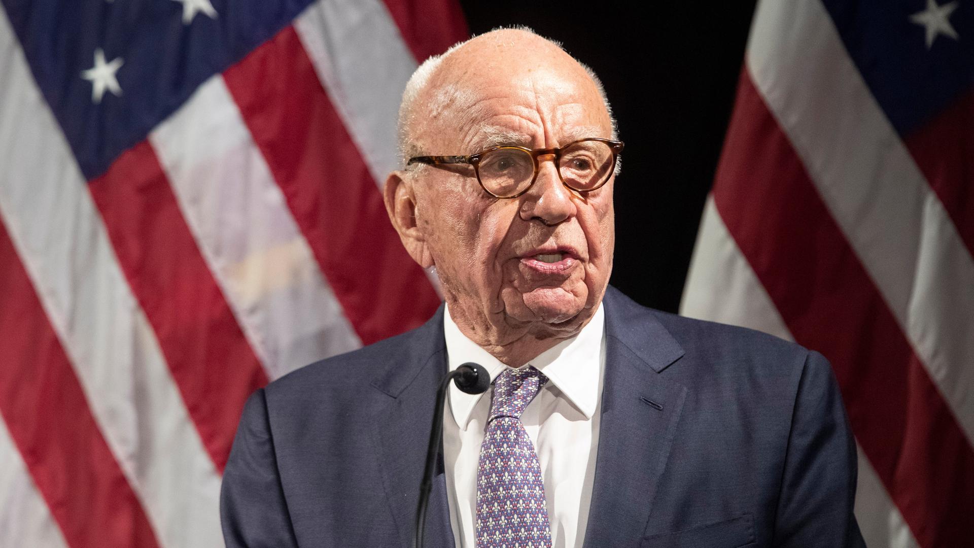 Rupert Murdoch steht am Mikrofon, hinter ihm eine US-amerikanische Flagge.