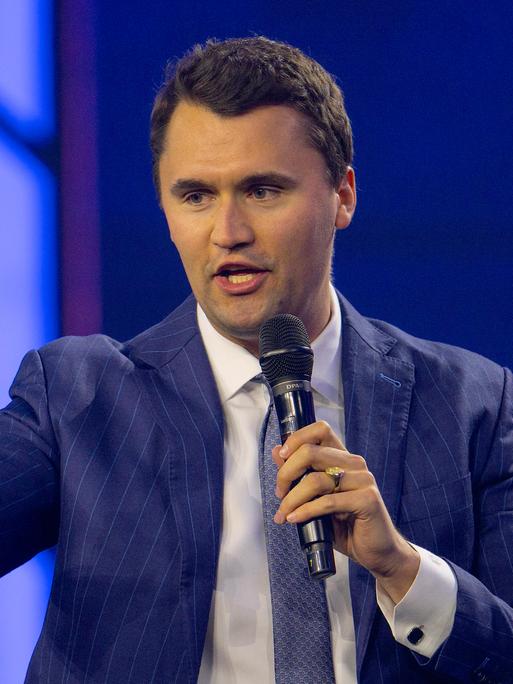 Charlie Kirk im blauen Anzug mit erhobenem Zeigefinger, während er in ein Mikrofon spricht. Charlie Kirk im blauen Anzug mit erhobenem Zeigefinger, während er in ein Mikrofon spricht.
