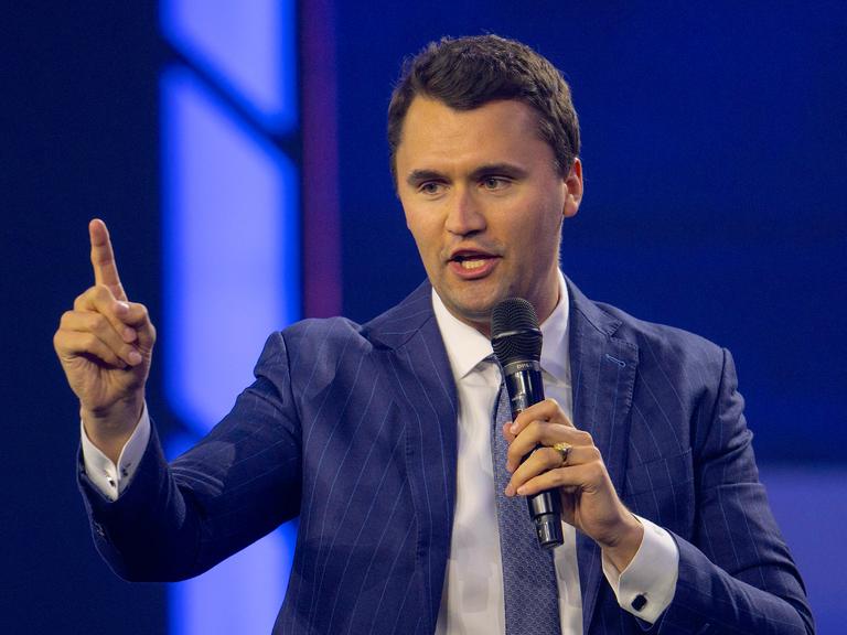 Charlie Kirk im blauen Anzug mit erhobenem Zeigefinger, während er in ein Mikrofon spricht. Charlie Kirk im blauen Anzug mit erhobenem Zeigefinger, während er in ein Mikrofon spricht.