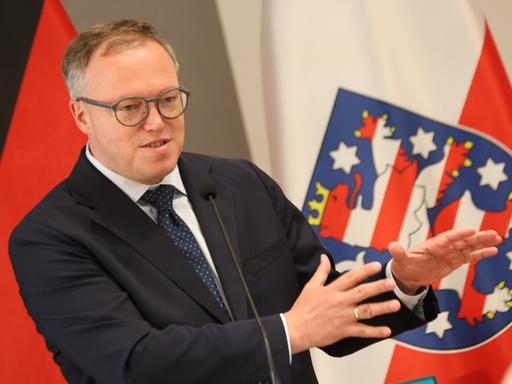 Thüringens Ministerpräsident Mario Voigt spricht vor der thüringischen Flagge 