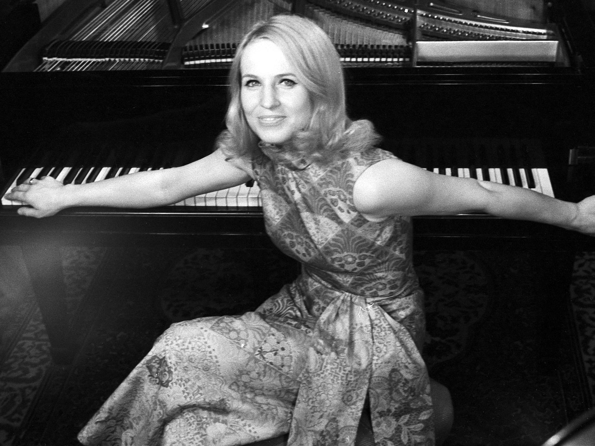 Schwarzweiß Bild der deutschen Pianistin und Hochschullehrerin Annerose Schmidt. Sie sitzt auf einem Hocker am Klavier und hat den Rücken zu dem Instrument gewandt und ihre Arme auf den Tasten ausgebreitet. 