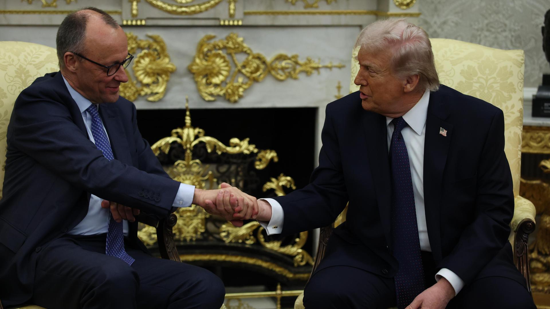 US-Präsident Donald Trump und Bundeskanzler Friedrich Merz sitzen nebeneinander und reichen sich die Hand 