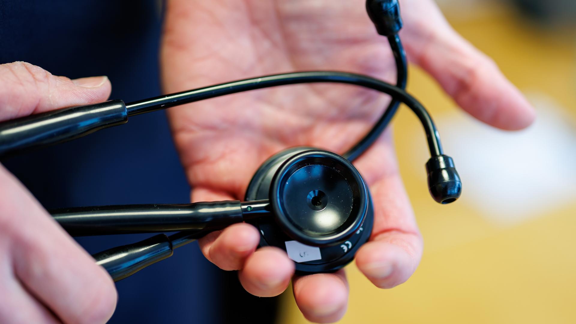 Zwei Hände halten ein schwarzes Stethoskop.