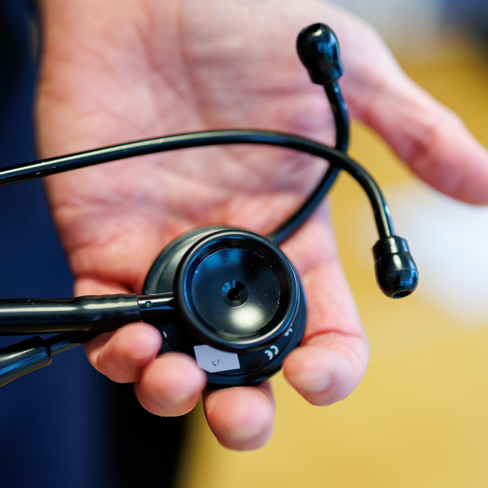 Zwei Hände halten ein schwarzes Stethoskop.