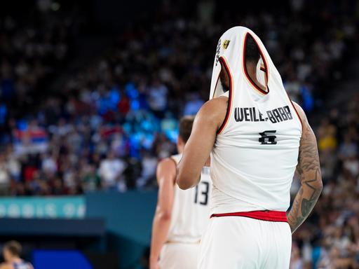 Der deutsche Basketball Nick Weiler-Babb zieht sich nach der Niederlage sein Trikot über den Kopf und versteckt so seinen Kopf. 