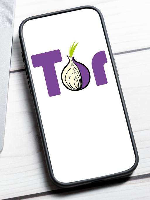 Das Tor-Netzwerk Logo wird auf einem Smartphone-Bildschirm neben einem Laptop angezeigt.