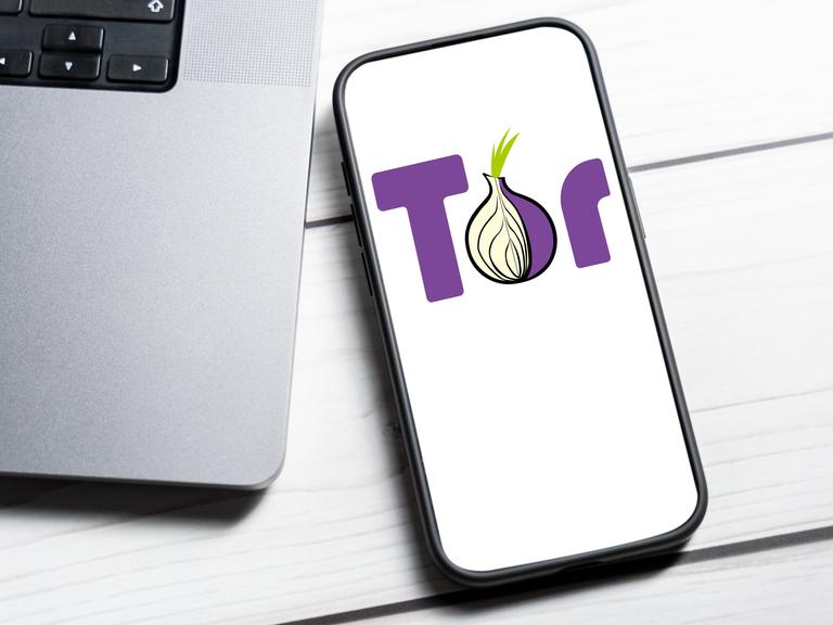 Das Tor-Netzwerk Logo wird auf einem Smartphone-Bildschirm neben einem Laptop angezeigt.