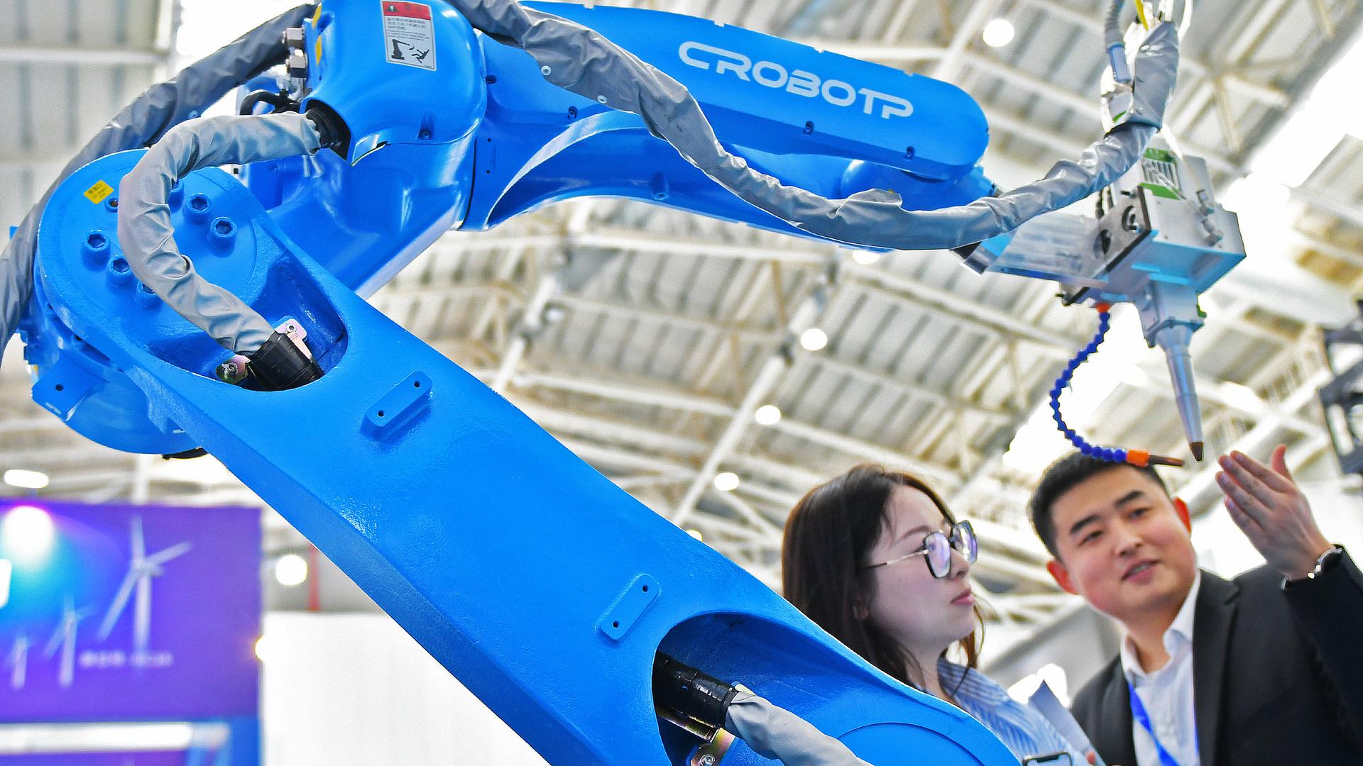 Zwei Besucher stehen auf der Internationalen Ausstellung Equipment Manufacturing in Yantai, China, neben dem Roboterarm einer automatisierten Schweißmaschine