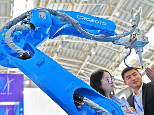 Zwei Besucher stehen auf der Internationalen Ausstellung Equipment Manufacturing in Yantai, China, neben dem Roboterarm einer automatisierten Schweißmaschine