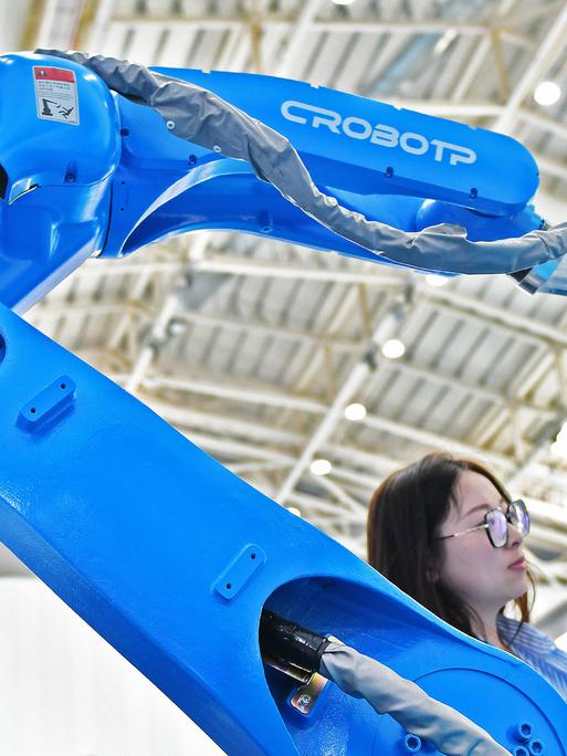 Zwei Besucher stehen auf der Internationalen Ausstellung Equipment Manufacturing in Yantai, China, neben dem Roboterarm einer automatisierten Schweißmaschine