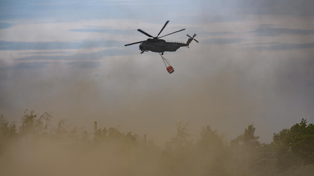 Ein Löschhubschrauber der Bundeswehr bei einem Waldbrand im Einsatz. An dem Hubschauber hängt ein Behälter für Löschwasser.