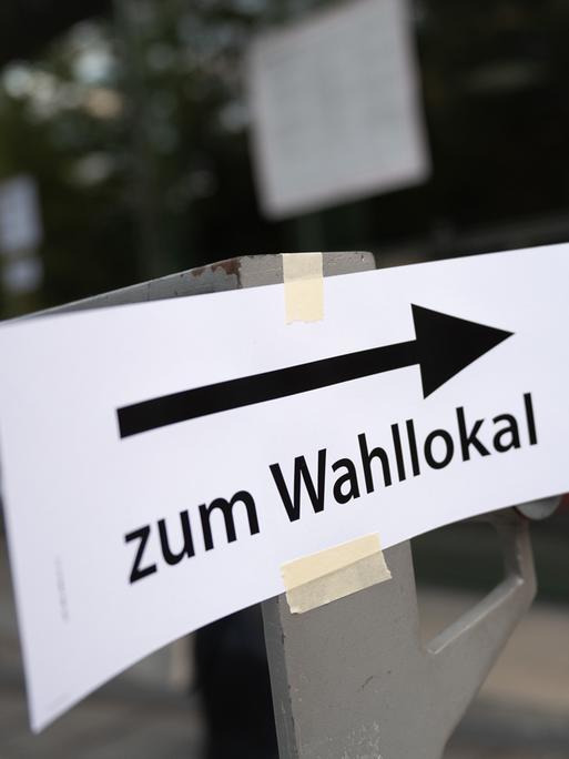 Ein Schild mit der Aufschrift "Zum Wahllokal" hängt vor einem Wahllokal. 