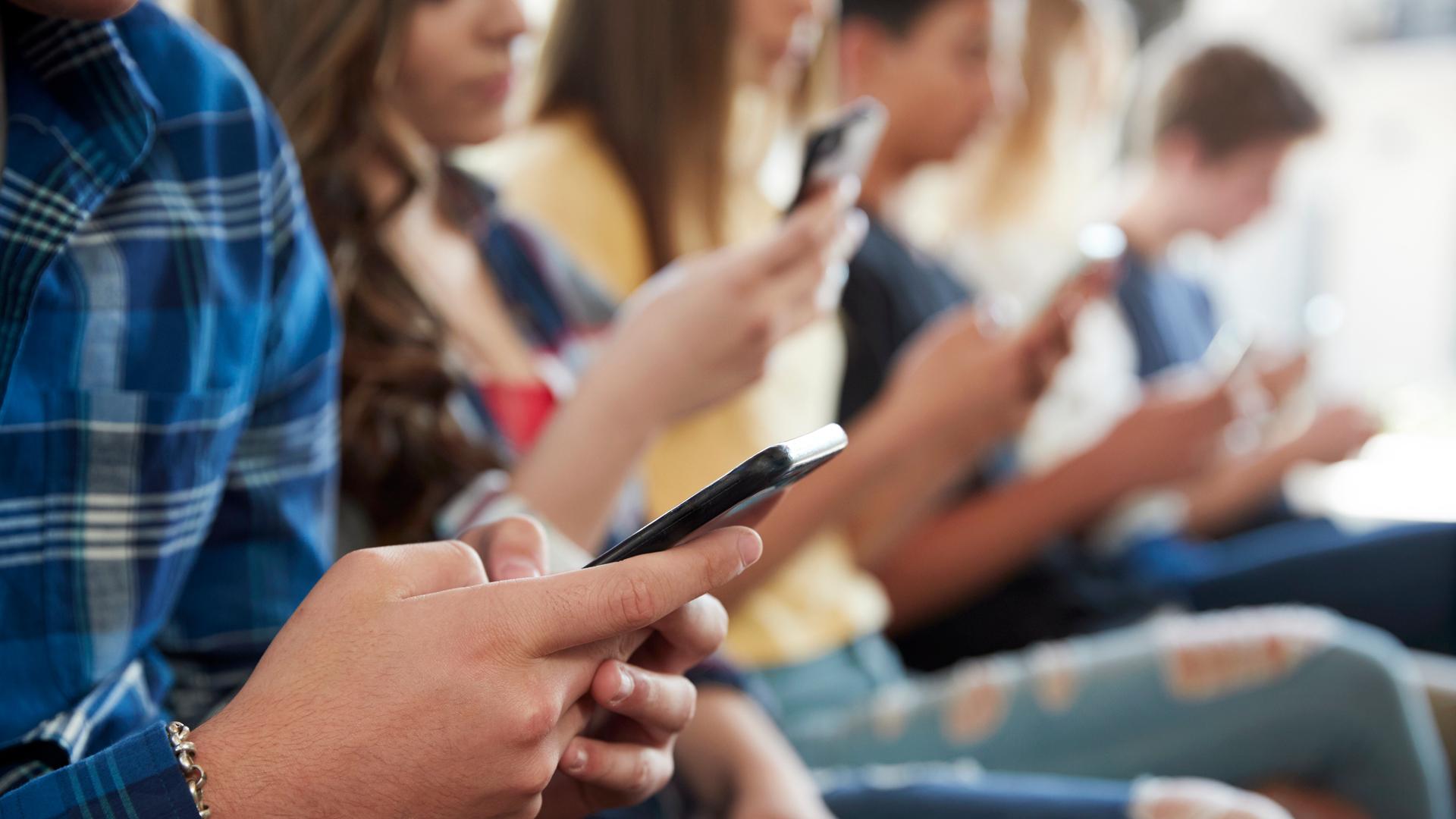 Jugendliche sitzen beisammen und schauen in ihre Smartphones Jugendliche sitzen beisammen und schauen in ihre Smartphones
