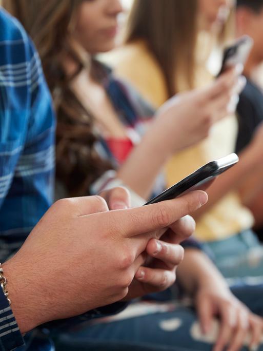Jugendliche sitzen beisammen und schauen in ihre Smartphones