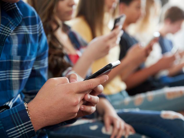 Jugendliche sitzen beisammen und schauen in ihre Smartphones