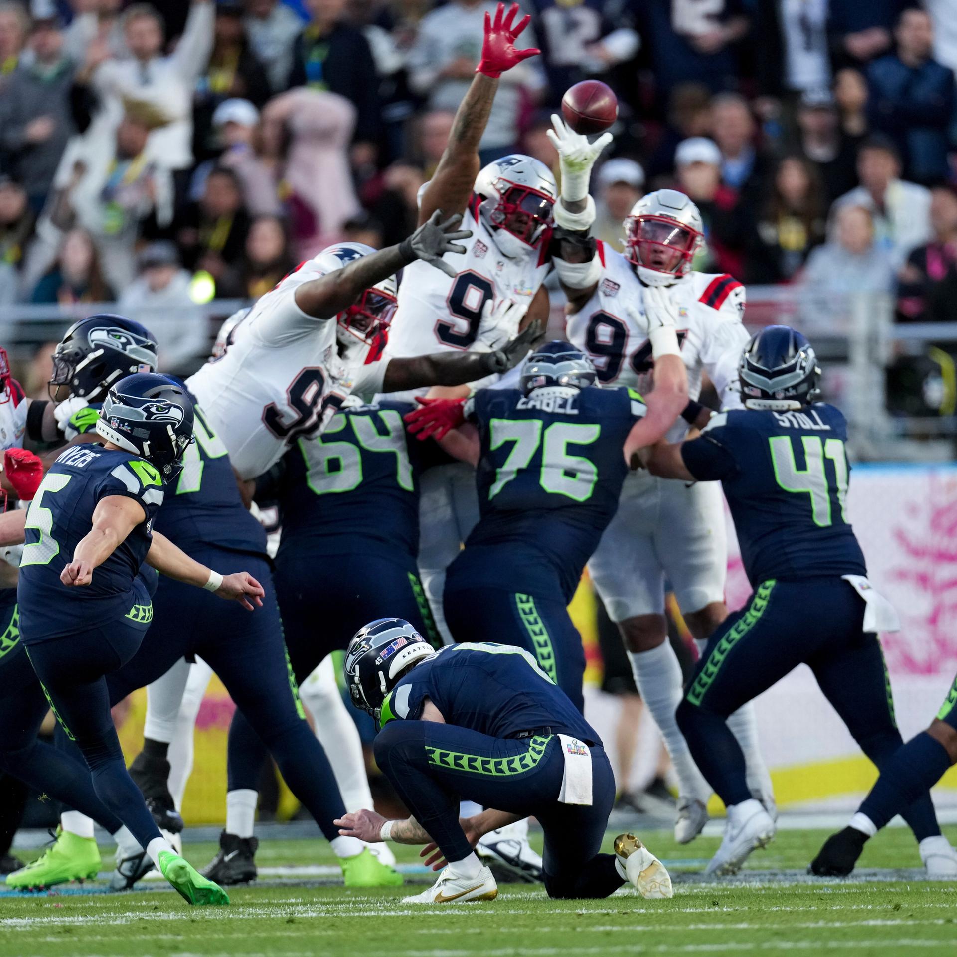 Das Bild zeigt viele American-Football-Spieler beider Teams in einer Art Gerangel um den Football. Sportarttypisch tragen sie schützende Helme und gepolsterte Kleidung.