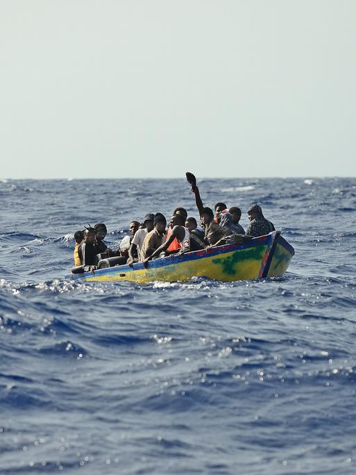 Ein Holzboot mit rund 30 Menschen treibt auf dem Meer