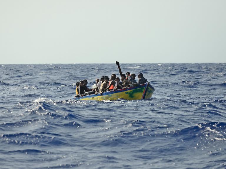 Ein Holzboot mit rund 30 Menschen treibt auf dem Meer