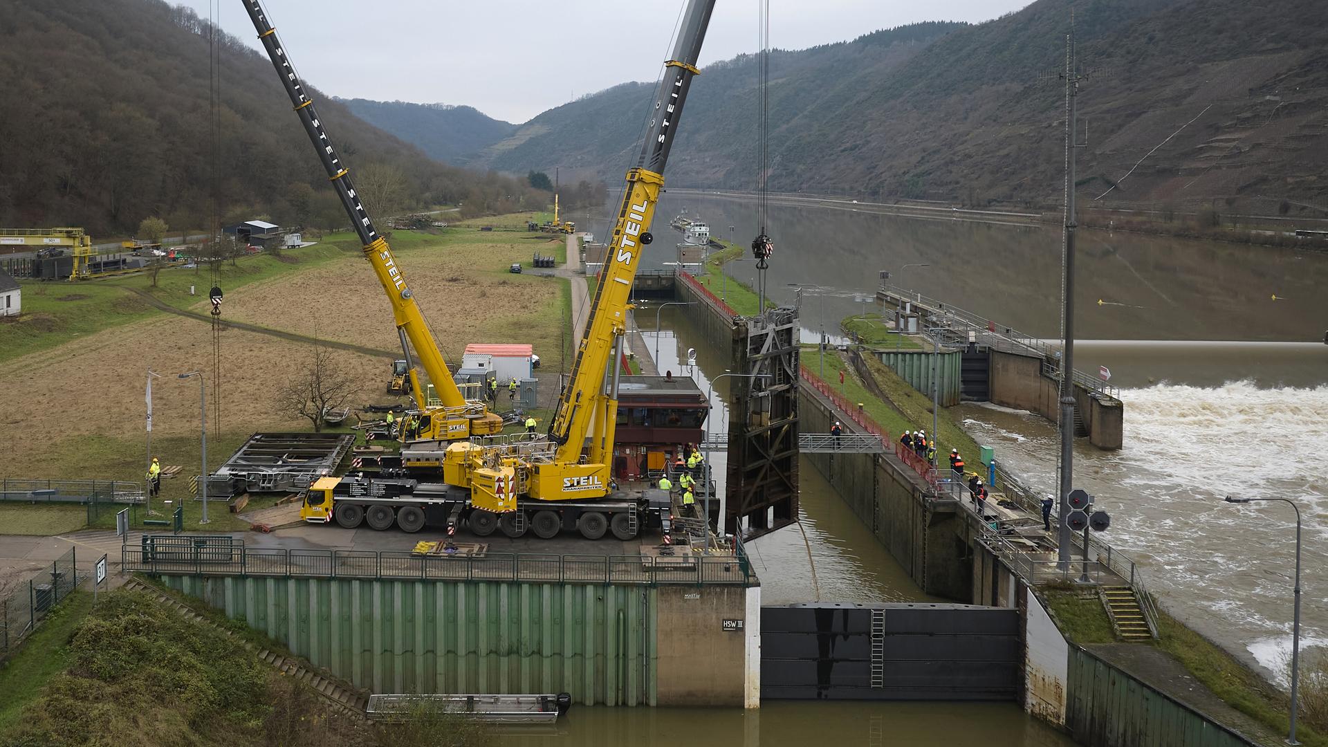 Zwei Kräne heben ein beschädigtes Schleusentor aus der Schleuse Müden. Seit dem 08.12. ist die Schifffahrt auf der Mosel lahmgelegt. Bei einer Kollision eines Frachtschiffs mit der Schleuse ist diese schwer beschädigt worden.