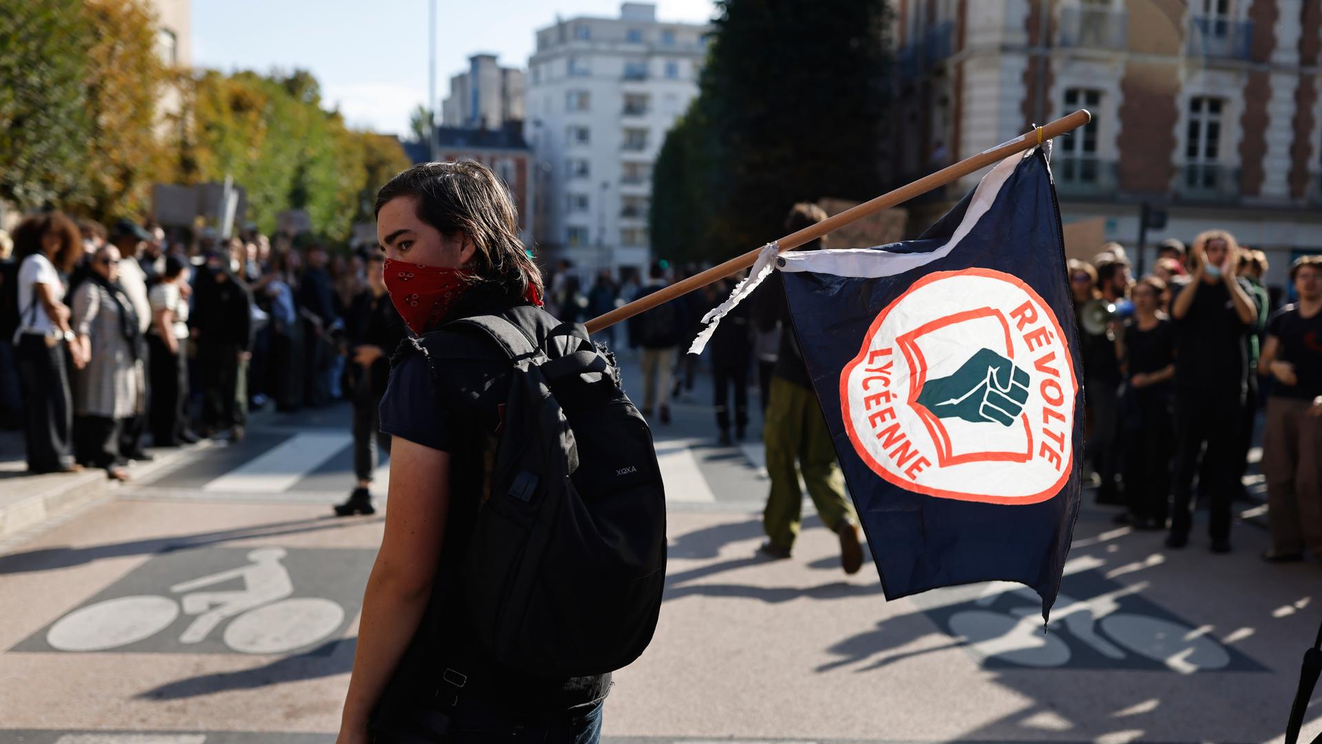 Ein Schüler mit halb vermummtem Gesicht trägt eine Fahne mit einem Logo der Schul-Proteste Ein Schüler mit halb vermummtem Gesicht trägt eine Fahne mit einem Logo der Schul-Proteste